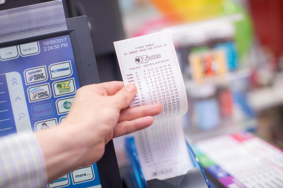 A man holds an Oz Lotto ticket in a newsagency.