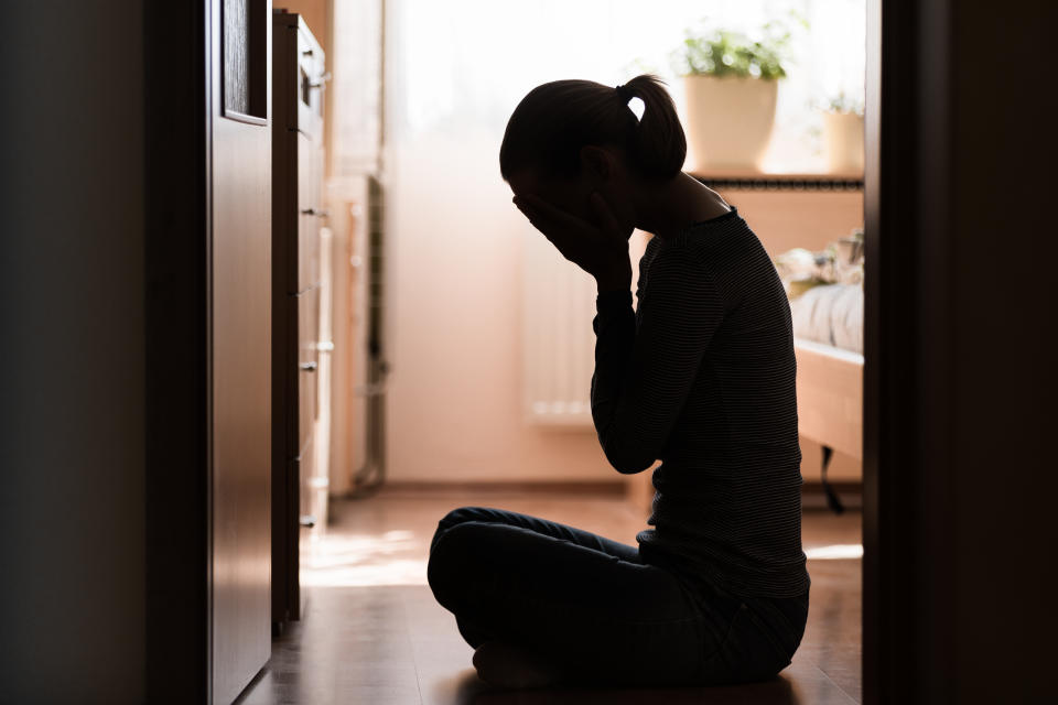 Sad young woman sitting on room floor crying with hand over face