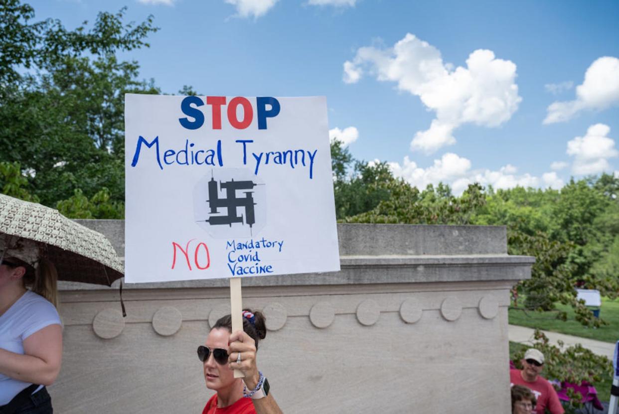 A woman holds a sign denouncing COVID-19 vaccine mandates, with syringes in the shape of a swastika, during a 2021 rally at the Kentucky Capitol in Frankfort. <a href="https://www.gettyimages.com/detail/news-photo/woman-holds-a-sign-denouncing-covid-19-vaccine-mandates-news-photo/1234925521?adppopup=true" rel="nofollow noopener" target="_blank" data-ylk="slk:Jon Cherry/Getty Images;elm:context_link;itc:0;sec:content-canvas" class="link ">Jon Cherry/Getty Images</a>