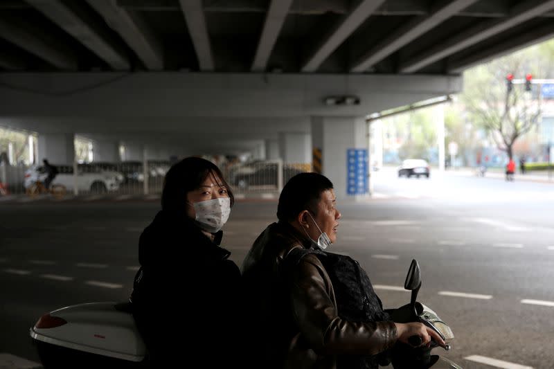 Woman wearing a face mask sits behind a man on a vehicle near Beijing's Financial Street in Beijing