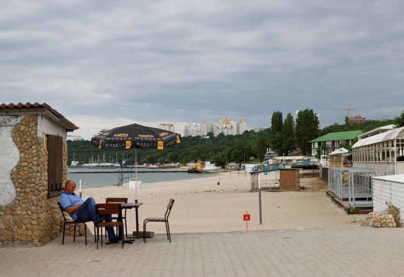 A man sits beside a closed off beach, in Odesa
