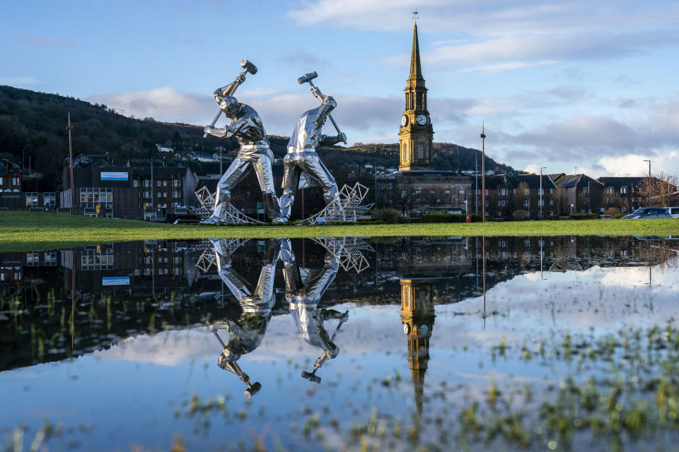 The Shipbuilders of Port Glasgow sculpture in Coronation Park, Inverclyde, is reflected in large puddles after heavy downpours, in Port Glasgow, Scotland, Friday Jan. 5, 2024. The impact of surface water and river flooding will continue to be "significant" across parts of the country following heavy rainfall, experts have warned. (Jane Barlow/PA via AP)