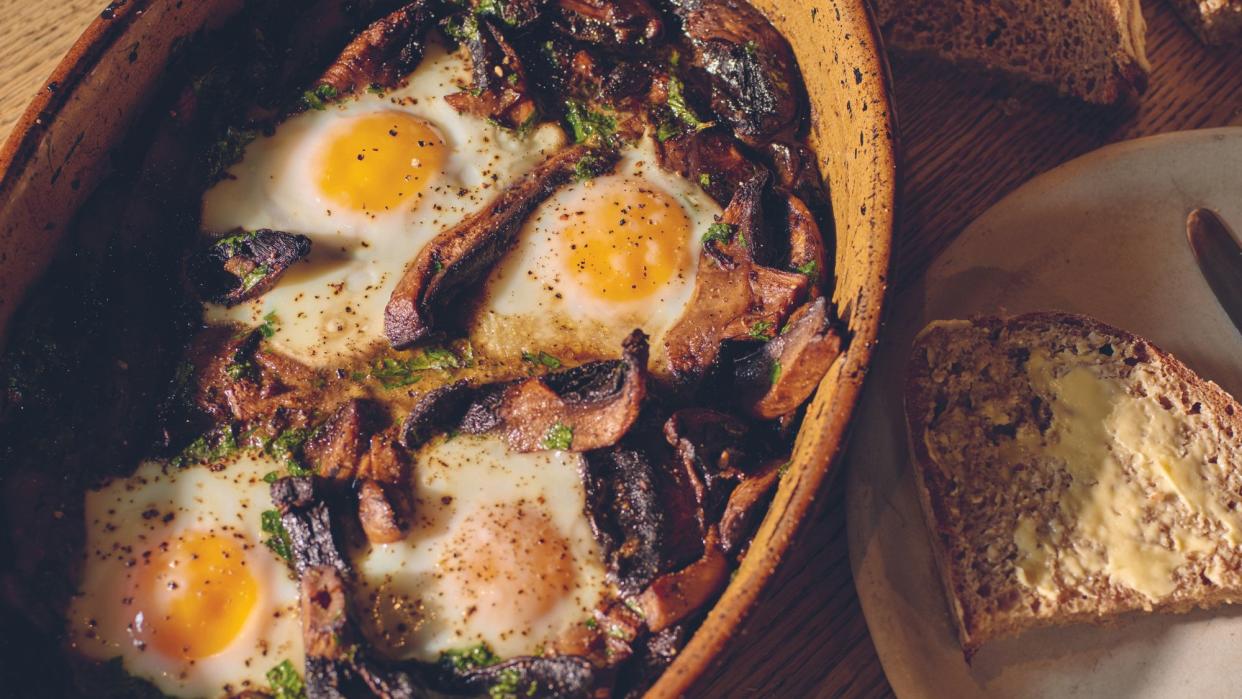  A dish of bake mushrooms with eggs next to a plate with buttered toast. 