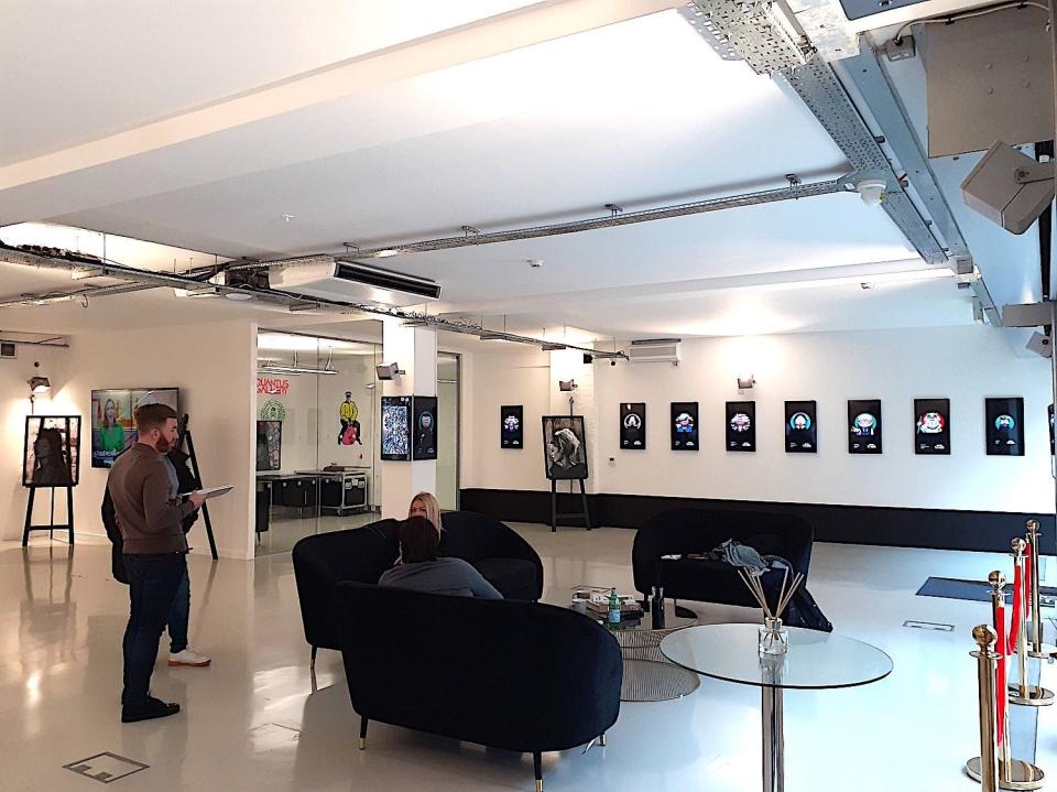 Quantus staff mingle on three sofas are positioned within the open-plan, single room. The back wall is adorned with TV screens featuring NFTs. There is also a physical piece of art in the far left corner.