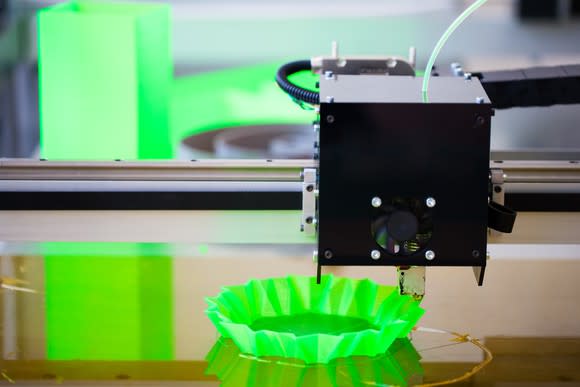 Close-up of a 3D printer head printing a unidentifiable, bright-green plastic object.