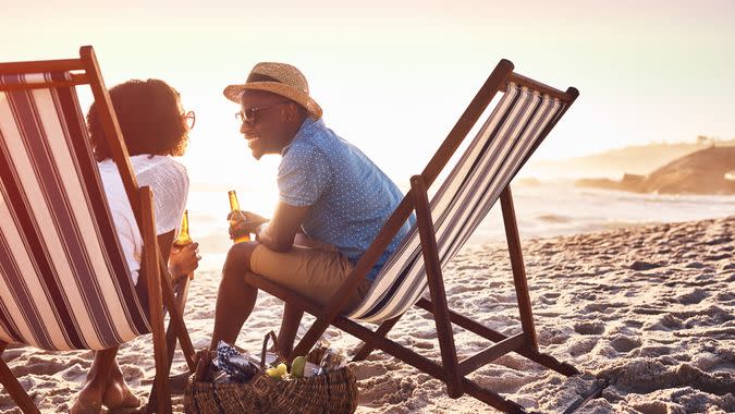 Shot of a happy young couple relaxing on chairs and having drinks at sunset on the beach.