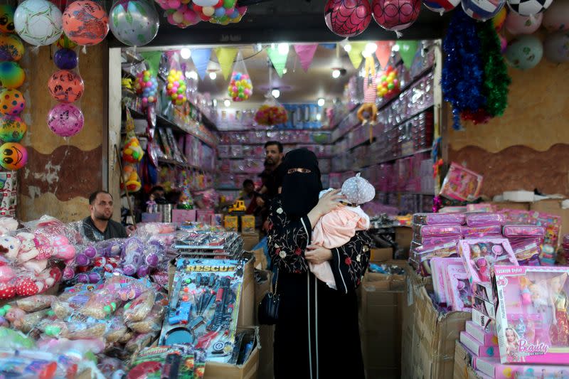 A woman holds her baby as she walks out of a toy store as Palestinians prepare for the upcoming holiday of Eid al-Fitr marking the end of Ramadan, amid concerns about the spread of the coronavirus disease
