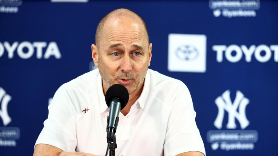 Brian Cashman speaks at the podium in a white polo with a blue background