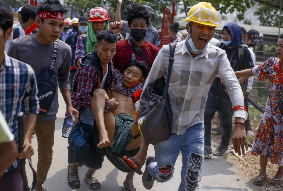 Anti-coup protesters carry an injured man following clashes with security in Yangon, Myanmar Sunday, March 14, 2021. The civilian leader of Myanmar's government in hiding vowed to continue supporting a "revolution" to oust the military that seized power in last month's coup, as security forces again met protesters with lethal forces, killing several people. (AP Photo)