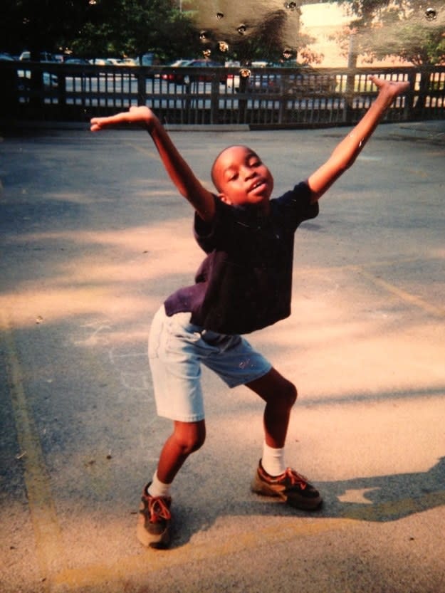 A young child in a playground and wearing a T-shirt and shorts strikes a pose and raises their hands in the air