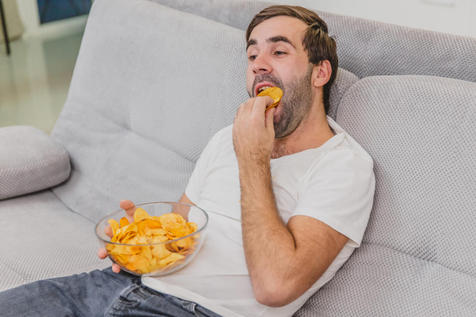 Mann auf Sofa isst Chips