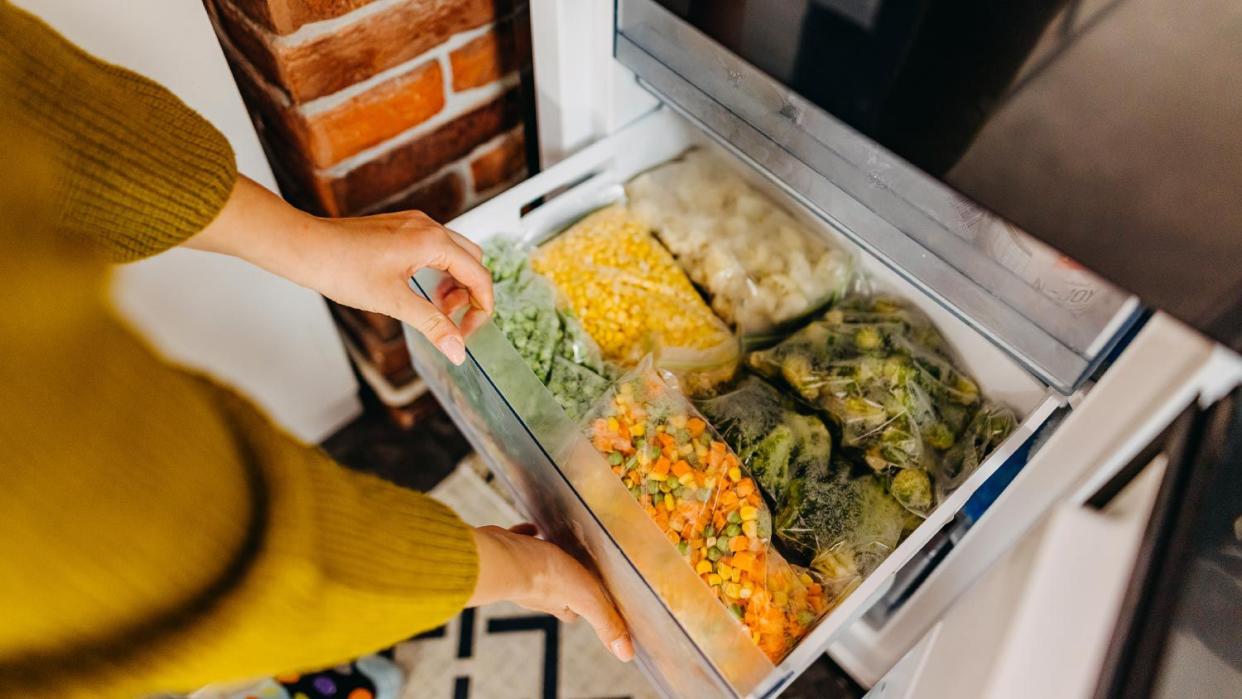 Woman putting container with frozen mixed vegetables