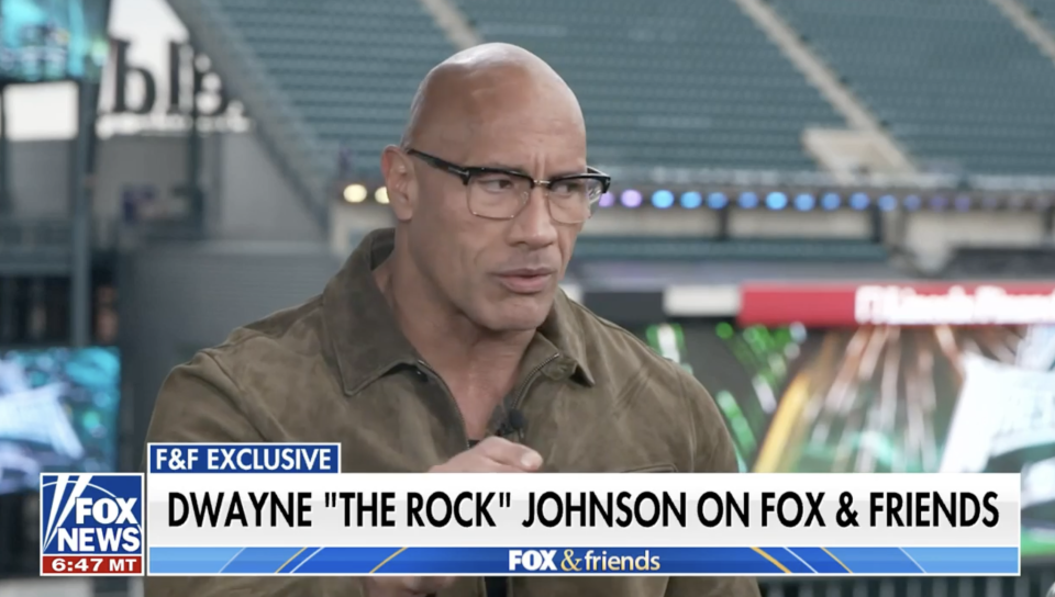 Dwayne Johnson in a TV interview wearing a brown shirt, in a studio setting