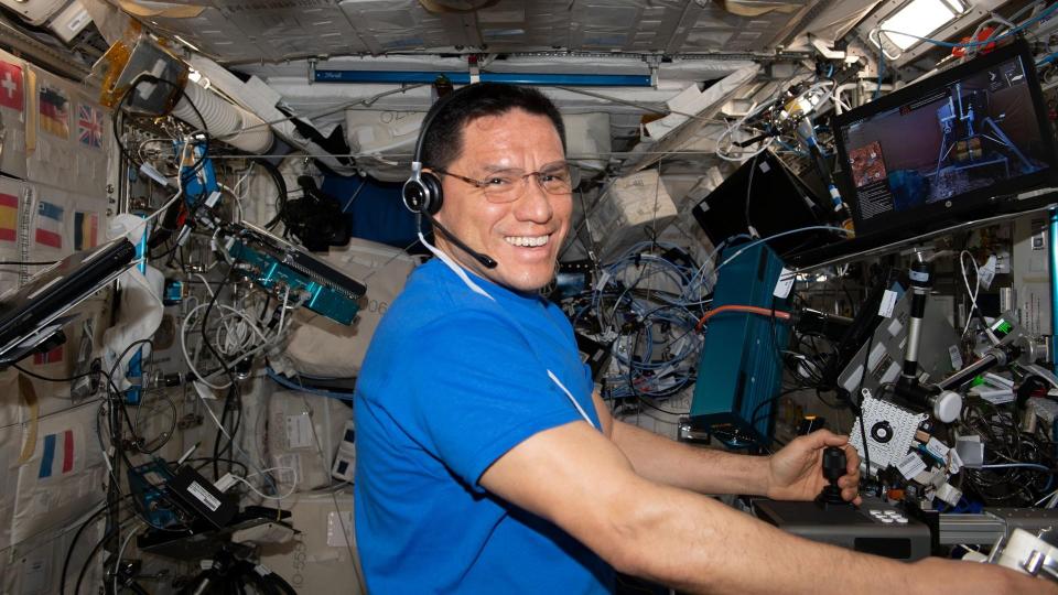 an astronaut floating in spies smiles as he handles lab equipment