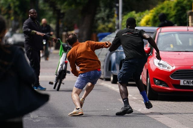 Man in orange top chases two men along a street