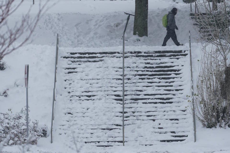 A pedestrian walks near a snow-covered staircase, Saturday, Feb. 13, 2021, on the University of Washington campus in Seattle. Winter weather was expected to continue through the weekend in the region.(AP Photo/Ted S. Warren)