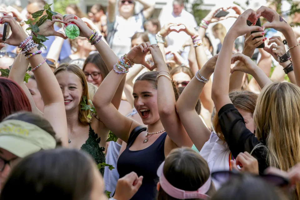 Several young people hold their hands above their heads making heart symbols.