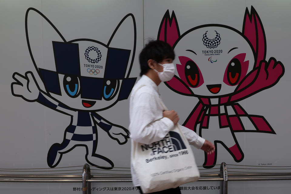 A man wearing a protective face mask walks past a mural featuring the mascots of the Tokyo 2020 Olympics and Paralympics 