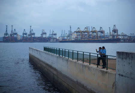 Security guards take a break as ships are seen unloading cargo in the background at Tanjong Pagar container terminal in Singapore March 9, 2015. REUTERS/Edgar Su/File Photo