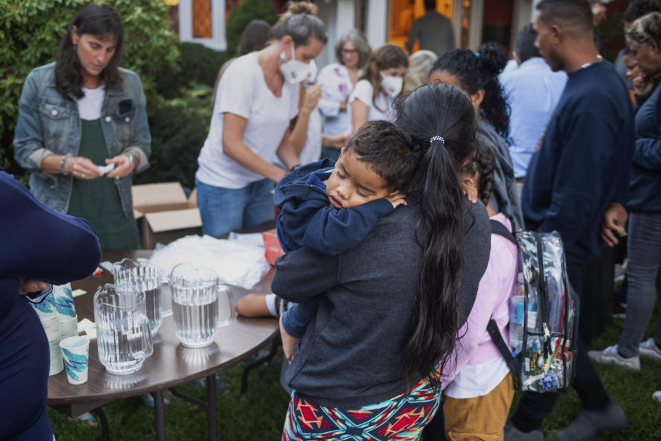 Una mujer, que está en un grupo de migrantes que fueron trasladados a Martha's Vineyard, Massachussets, carga a su hijo mientras son alimentados afuera de una iglesia. (Ray Ewing/Vineyard Gazette vía AP)