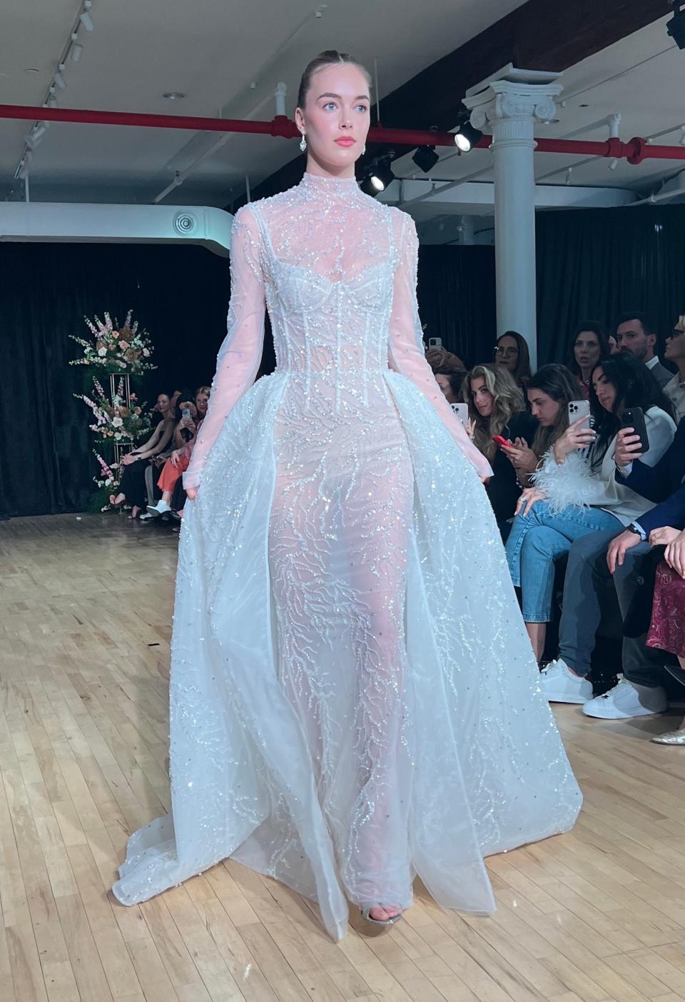 A woman walks in a sheer, sparkly wedding dress.
