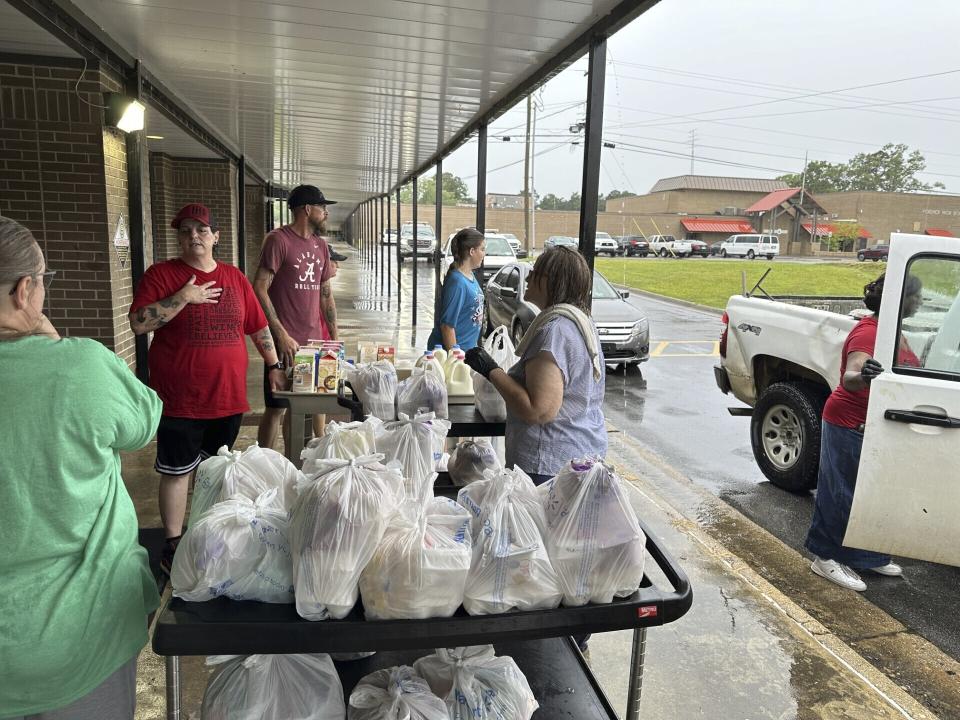 Volunteers hand out bags of groceries and jugs of milk to cars lined up at Fordyce High School in Fordyce, Arkansas on Wednesday, June 26, 2024. The school is one of several food distribution sites that have been set up to help residents after a mass shooting at the Mad Butcher grocery store. (AP Photo/Andrew DeMillo)