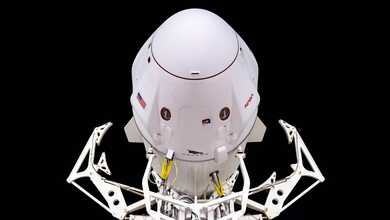  a white spacex dragon capsule is seen head-on with dark skies in the background. 