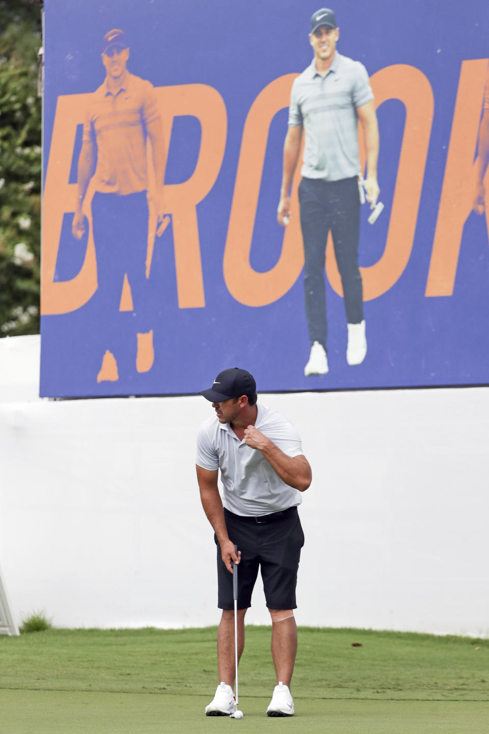 Brooks Koepka putts on the practice green under a banner with his picture at the World Golf Championship-FedEx St. Jude Invitational Wednesday, July 29, 2020, in Memphis, Tenn. Koepka, who won three times last year is trying to defend his FedEx St. Jude Invitational title with an injured left knee that has had him putting more weight on his right leg and affecting his game. (AP Photo/Mark Humphrey)