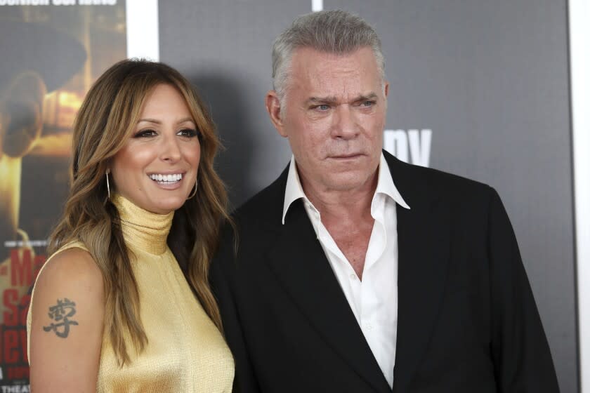 A woman in a gold dress and a man in a black suit posing for a photo