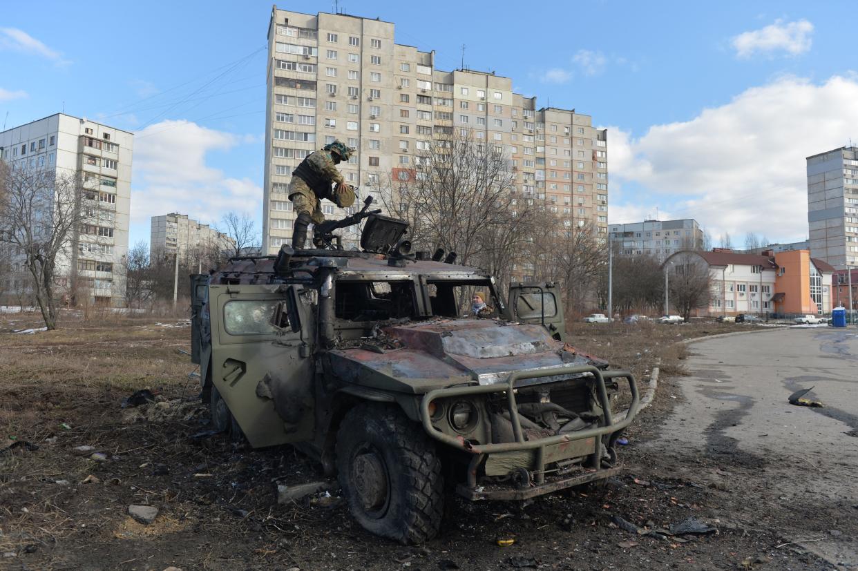 A Ukrainian fighter examines a destroyed Russian infantry mobility vehicle.