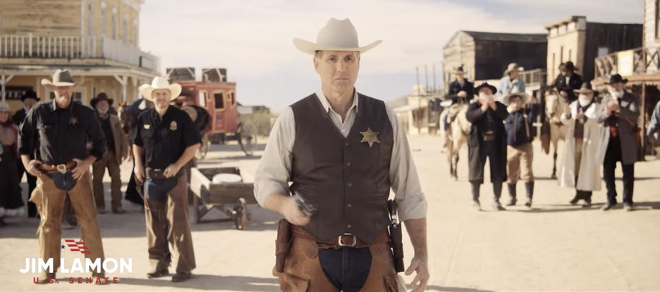 A Jim Lamon for U.S. Senate Super Bowl Ad shows Lamon dressed in a cowboy hat with a sheriff's badge pointing a handgun at the camera, surrounded by townspeople on a Wild West set.