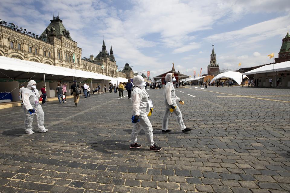 Volunteers wearing face masks, gloves and protective gear to protect against coronavirus, preapre to clean an area of an outdoor book market set up at Red Square with GUM, State Department store, left, St. Basil's Cathedral, center, Spasskaya Tower, second with, and the Kremlin Wall, right, in Moscow, Russia, Saturday, June 6, 2020. Muscovites clad in face masks and gloves ventured into Red Square for an outdoor book market, a small sign of the Russian capital's gradual efforts to open up amid coronavirus concerns. (AP Photo/Alexander Zemlianichenko)