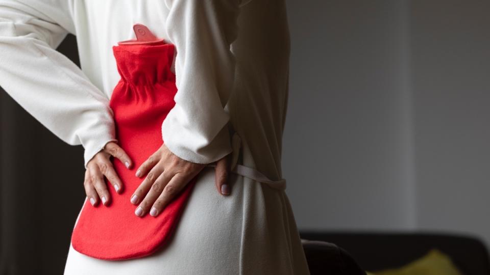 A woman in a white robe using a read heat pad for sciatica after using ice