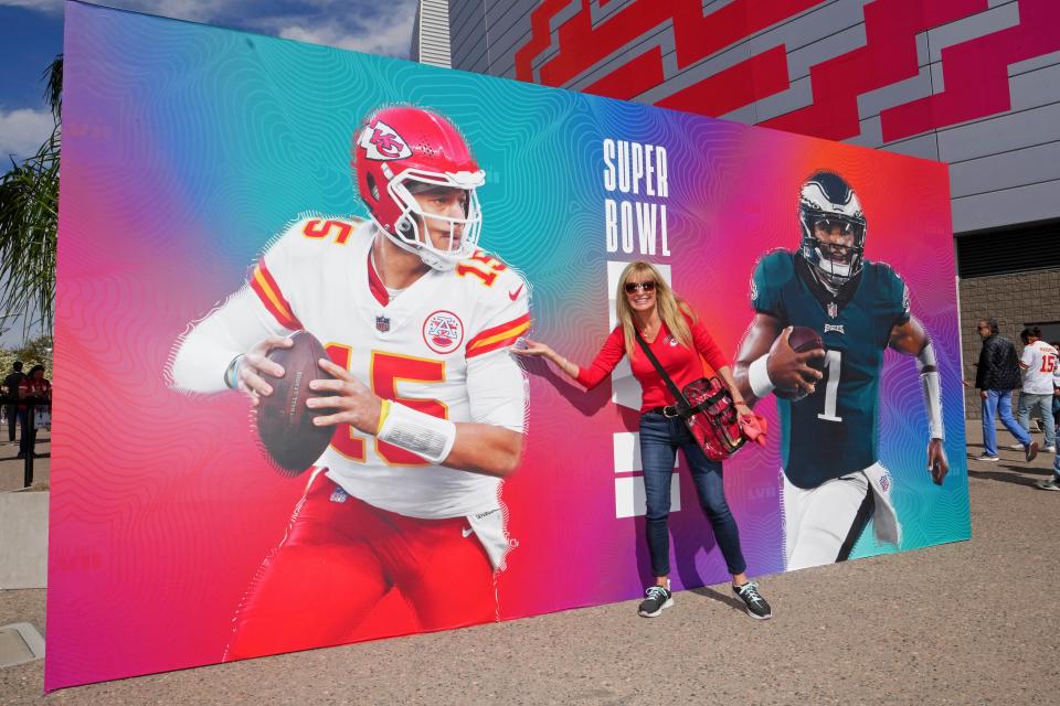 A Kansas City Chiefs fan poses in front of a sign promoting Super Bowl 57 quarterbacks Patrick Mahomes and Jalen Hurts outside State Farm Stadium.