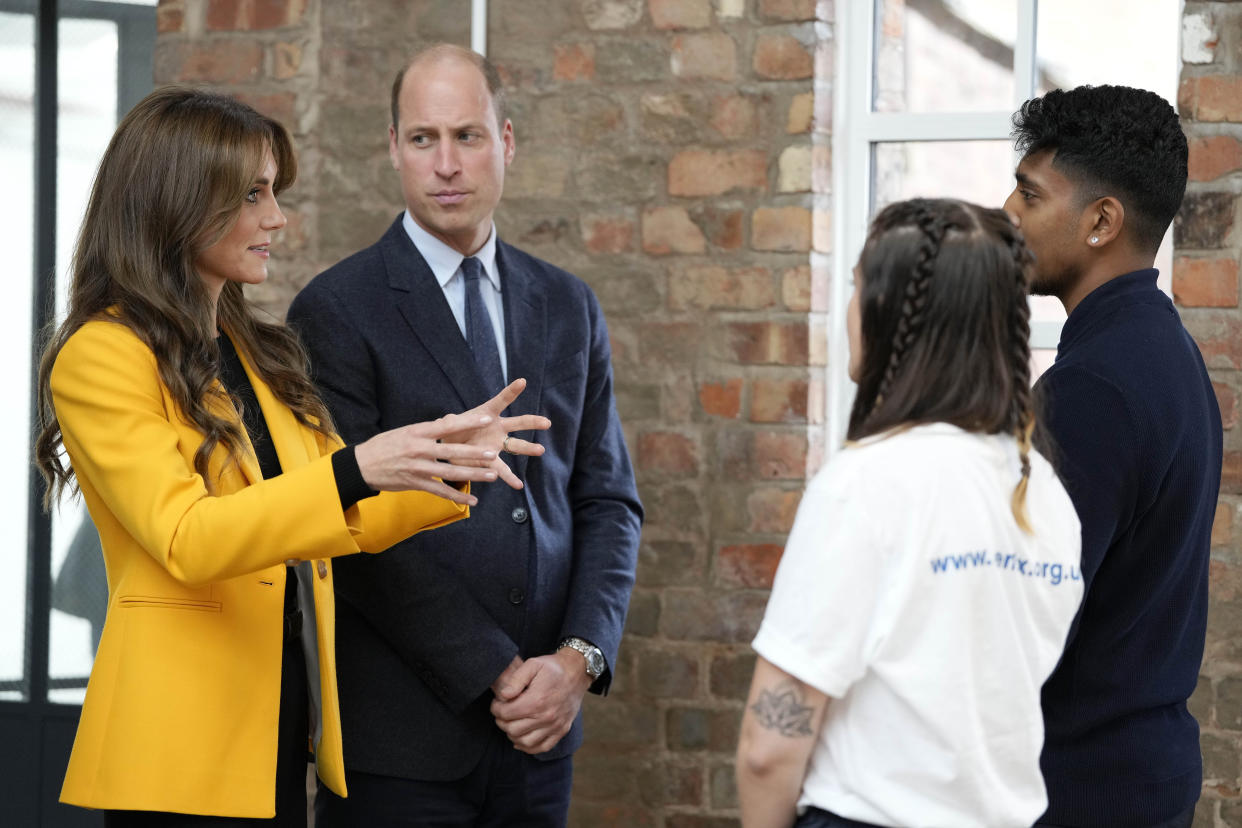 Prince William, wearing a suit and tie, and Kate Middleton, wearing a yellow blazer over a black top, speak to young people as they participate in a series of workshops which focus on emotions, relationships and community action