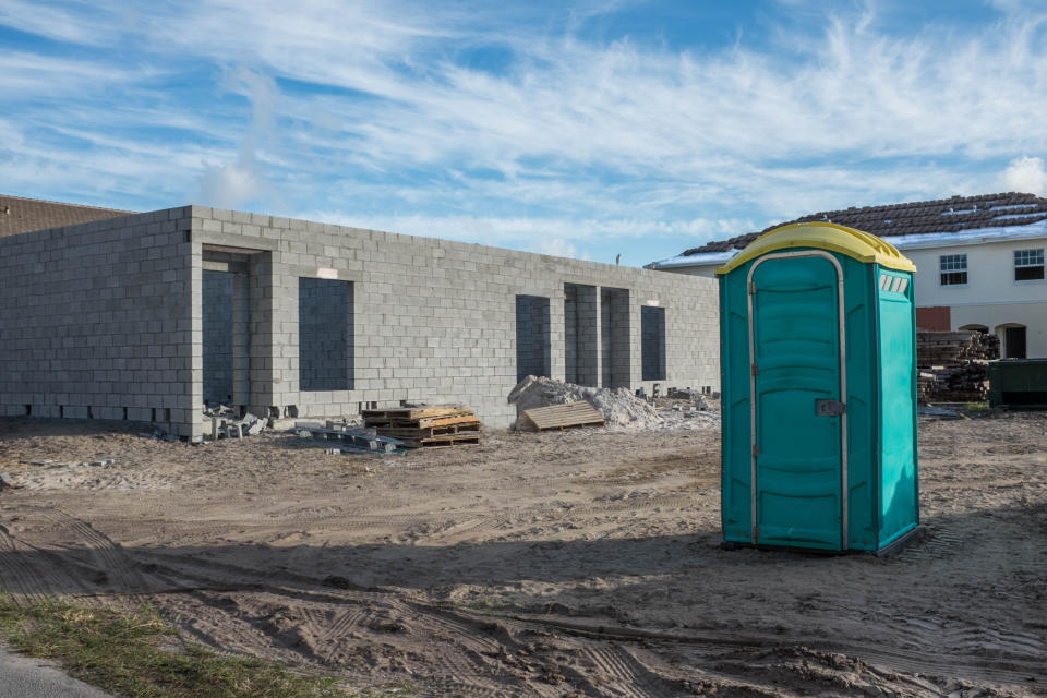 Green portable toilet for workers on the unpaved dirt section of a construction zone.