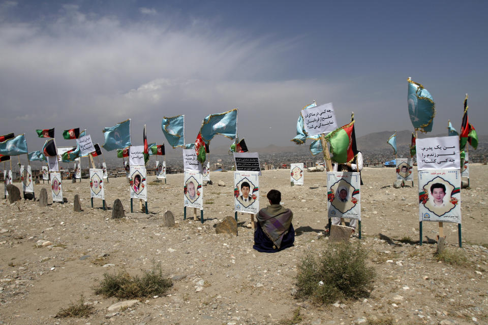 An Afghan young boy site near to the grave of his classmate, adorned with his picture, on the outskirts of Kabul, Afghanistan, Monday, Sept 14, 2020. Scores of friends and families of students who were killed in local conflicts are gathering in a cemetery to call for a permanent countrywide ceasefire from the parties to the intra-Afghan peace conference taking place in Doha, Qatar. (AP Photo/Rahmat Gul)