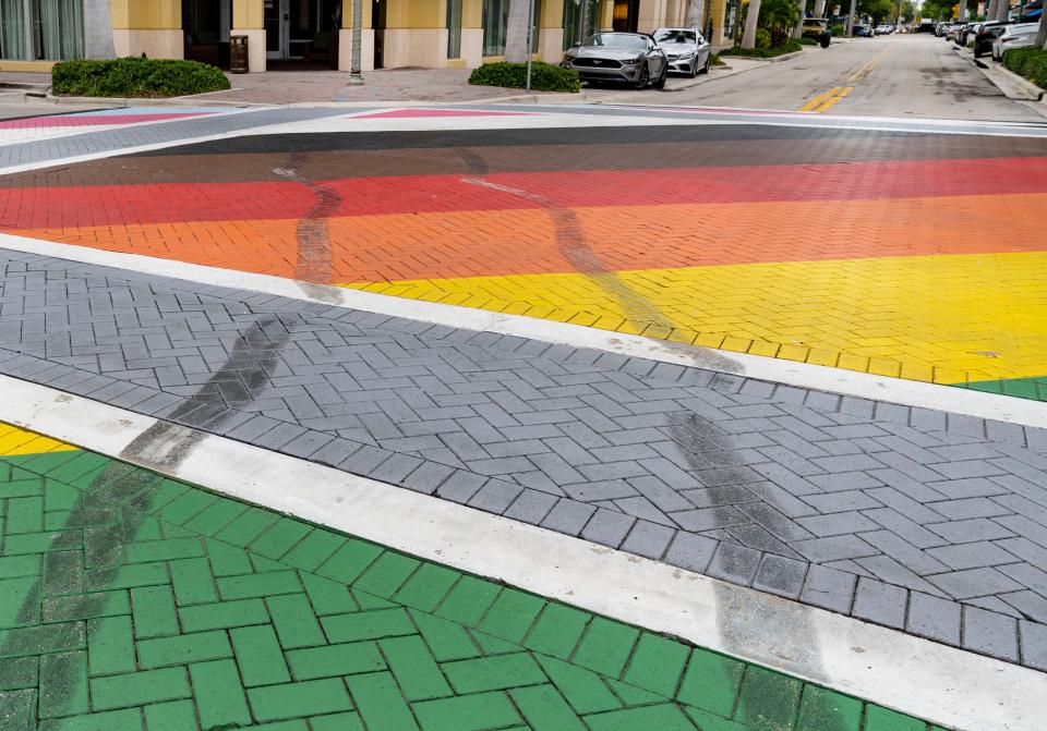 A man rides his scooter past the damage done to a LGBTQ Pride intersection and crosswalk that a driver vandalized in Delray Beach, Florida on June 18, 2021. Alexander Jerich, 20, was charged with criminal mischief over $1,000, reckless driving and evidence of prejudice (felony enhancement).