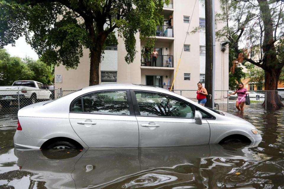 Una pareja de mujeres camina junto a un automóvil estacionado en la esquina inundada de SW 8 Avenue y 4th Street mientras los vecinos observan desde un balcón en el vecindario de Little Havana en Miami, Florida, el sábado 4 de junio de 2022.