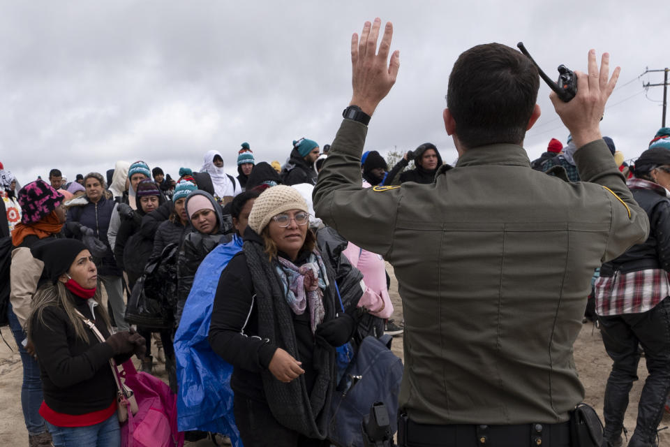 La peruana Julia Paredes, a la izquierda con un gorro blanco, escucha las instrucciones de un agente de la patrulla fronteriza junto a otros solicitantes de asilo, mientras esperan a ser procesados tras cruzar la cercana frontera con México, el jueves 25 de abril de 2024, en Boulevard, California. México empezó a requerir visas a los peruanos en respuesta al aluvión de migrantes del país suramericano, tras tomar medidas idénticas para venezolanos, ecuatorianos y brasileños, lo que en la práctica eliminó la opción de viajar en avión a una ciudad mexicana cerca de la frontera estadounidense. (AP Foto/Gregory Bull)