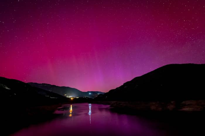 Aurora borealis reflected over a tranquil river with mountains and a glowing horizon