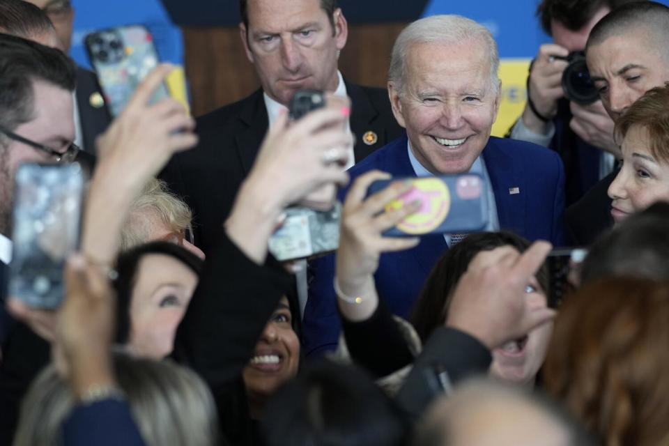 President Biden, surrounded by supporters, smiles for those taking selfies with him in the background