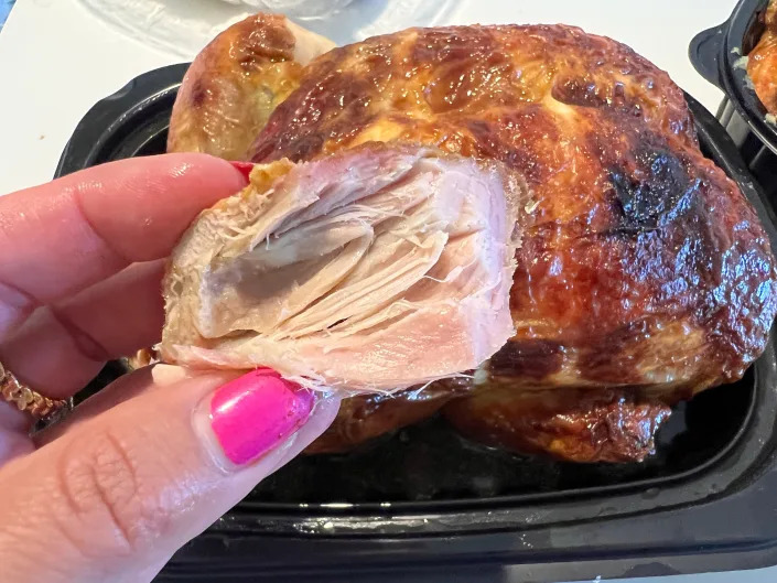 The writer holds a piece of leg meat from Costco rotisserie chicken