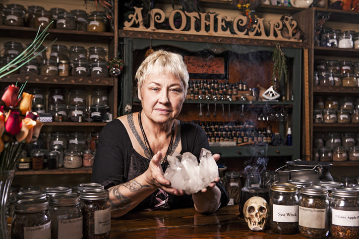 Women in an apothecary shop holding crystals and surrounded by jars of herbs