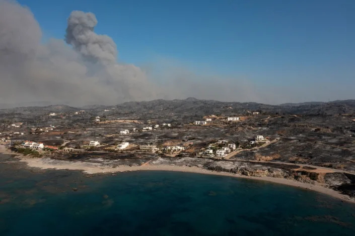 TOPSHOT - An aerial view shows smoke billowing in background of Kiotari village, on the island of Rhodes on July 24, 2023. Tens of thousands of people have already fled blazes on the island of Rhodes, with many frightened tourists scrambling to get home.
Greece has been sweltering under a lengthy spell of extreme heat that has exacerbated wildfire risk and left visitors stranded in peak tourist season. (Photo by Spyros BAKALIS / AFP) (Photo by SPYROS BAKALIS/AFP via Getty Images)