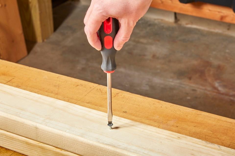 A person using a flathead screwdriver to remove a stripped screw stuck in a wood stud.