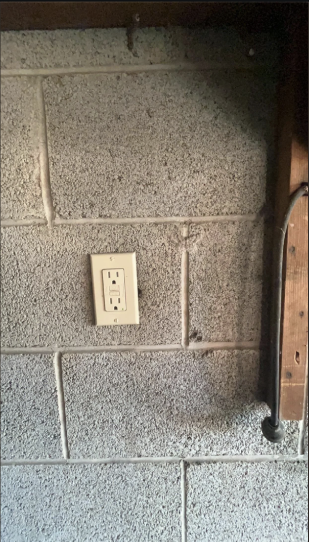 Electrical outlet on a concrete block wall with some exposed wooden framing and piping