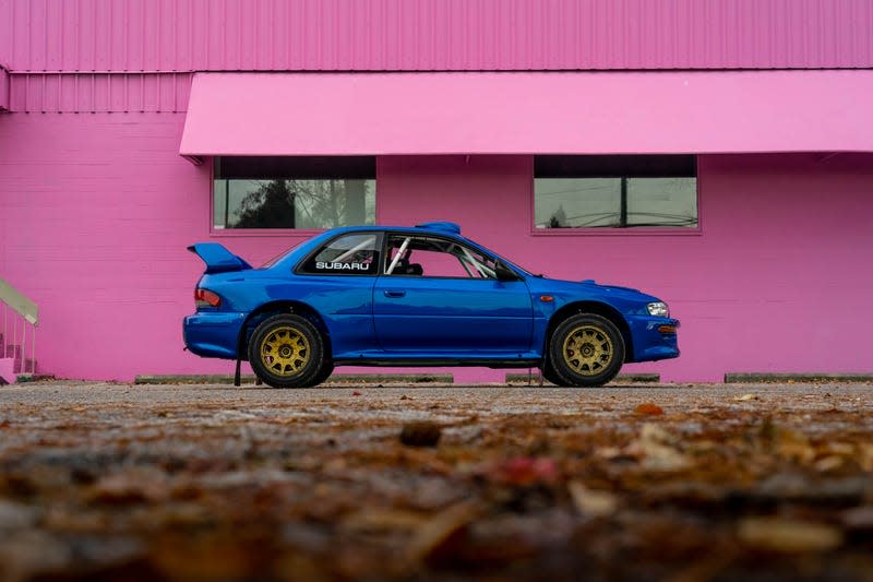 side profile photo of a blue subaru 2.5rs parked in front of a bright pink building
