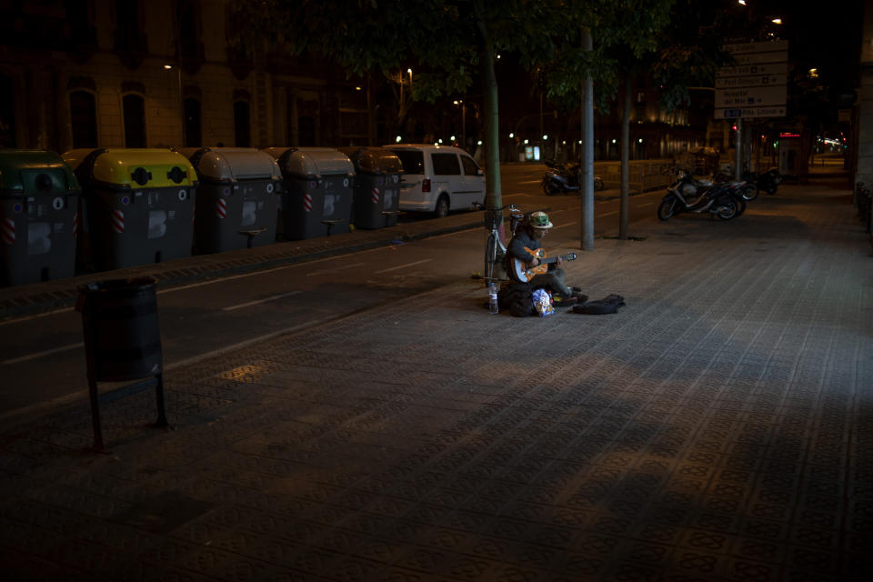 In this Saturday, March 21, 2020 photo, Kevin, 32, from France, plays guitar in front of a supermarket in Barcelona, Spain. Kevin, who has slept on the streets of Barcelona for the last 4 years said "I used to earn enough money to eat every day, now I don't get even one meal a day. Now I play the guitar just for me as nobody is in the street". While Spanish authorities tell the public that staying home is the best way to beat the coronavirus pandemic, some people are staying out because home has come to mean the streets of Madrid and Barcelona. (AP Photo/Emilio Morenatti)