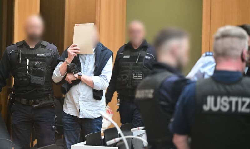 A defendant is led into the courtroom in Stuttgart-Stammheim at the start of a trial for "Reich Citizens" who are alleged to have planned a coup in Germany. The Higher Regional Court is trying nine defendants from the alleged "Reichsbuerger" group around Heinrich XIII Prince Reuss, who himself will only be tried later in Frankfurt. Bernd Weißbrod/dpa-Pool/dpa